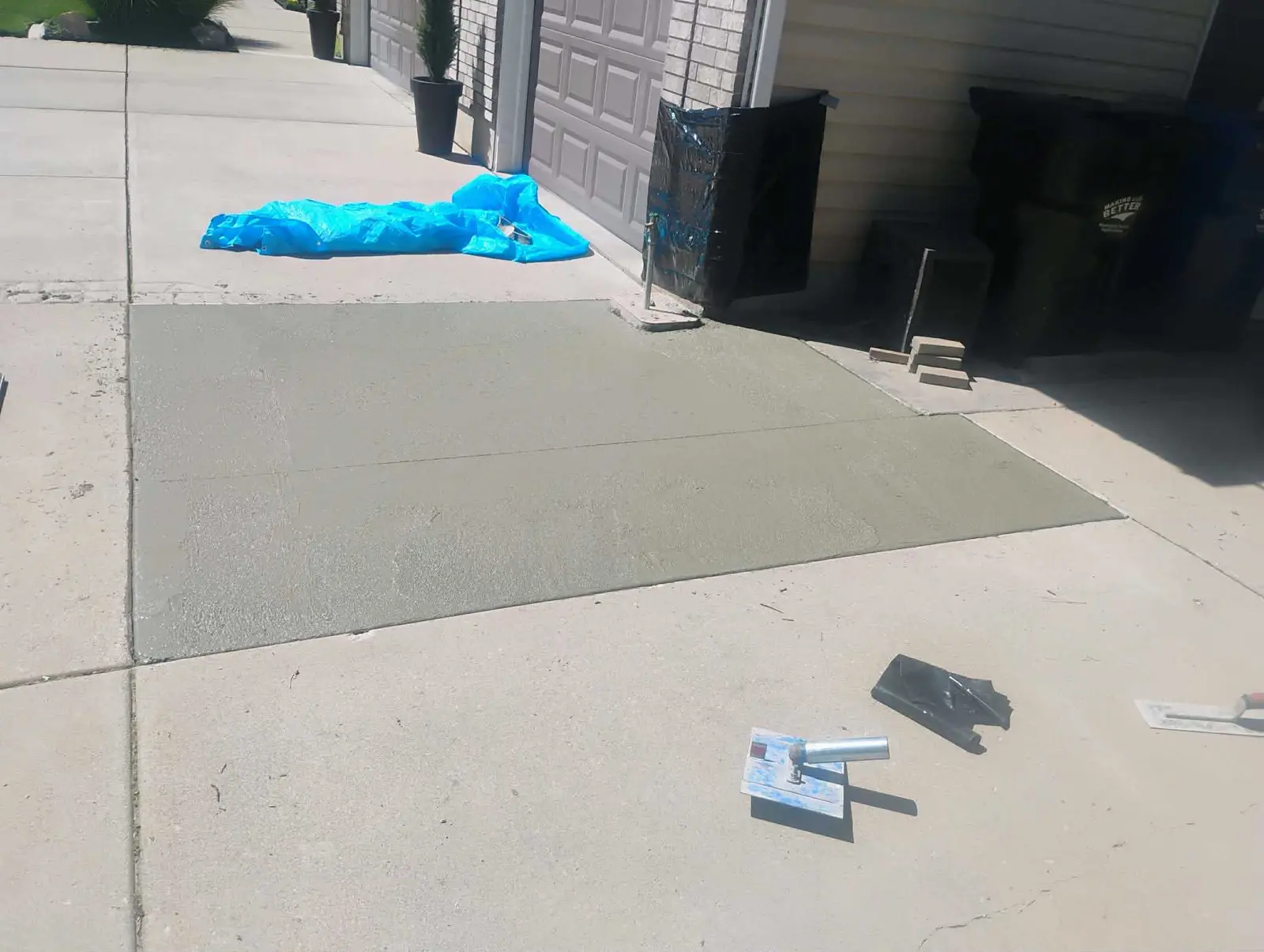 Freshly poured rectangular concrete section beside a brick home