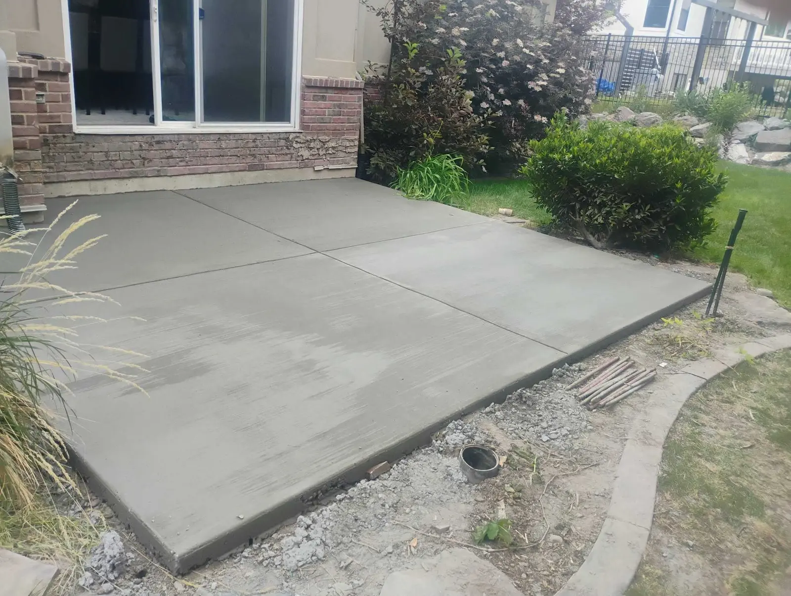 Completed concrete patio beside a brick home and landscaped yard